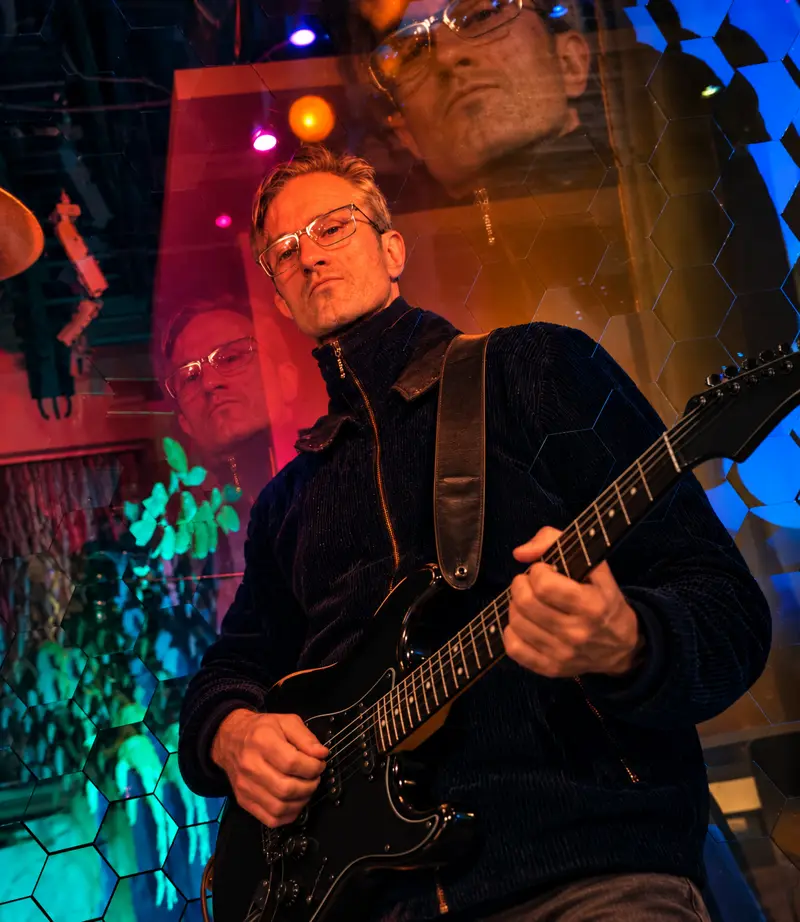 Chris playing electric guitar on stage under colored lights