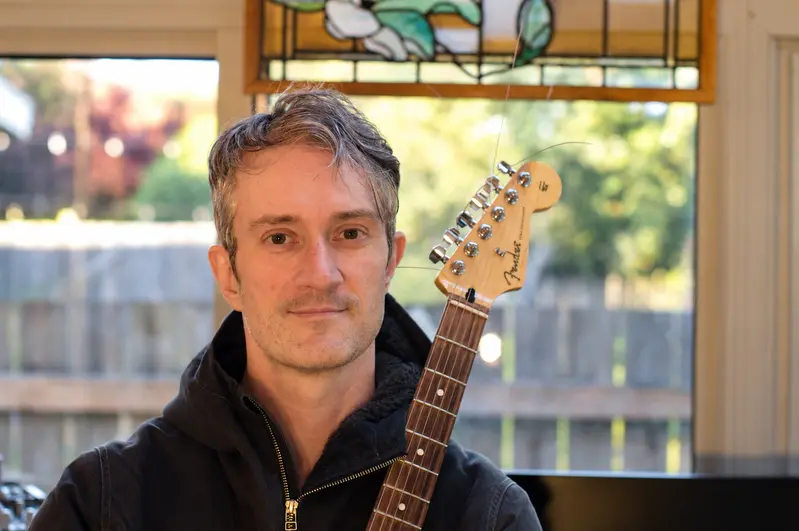Chris holding a guitar in his West Seattle studio
